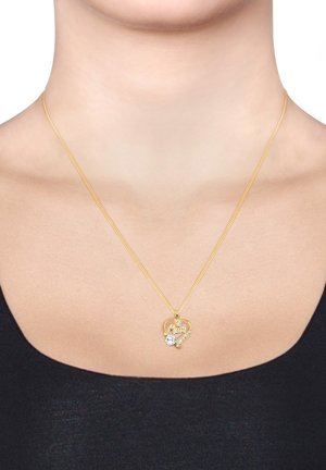 Eine goldfarbene Halskette mit einem herzförmigen Anhänger, auf dem "Mama" eingraviert ist, und einem kleinen klaren Steinchen als Akzent, getragen auf einem schwarzen Oberteil.