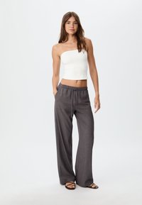 White strapless top with a fitted design paired with loose, dark gray, drawstring pants featuring a subtle texture. Model stands against a light background.