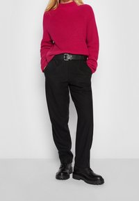 Gruby magenta sweter, czarne zwężające się spodnie i czarne buty nawiązujące z grubą podeszwą. Pasek podkreśla talię, tworząc podwyższoną sylwetkę.