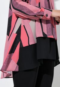 Lyserød og sort mønstret bluse med lange ærmer og hi-lo kant, lagdelt over en ensfarvet sort top, lavet af let stof.