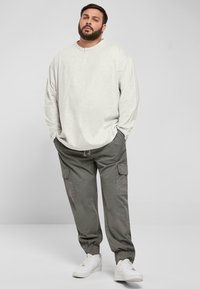 Lys grå langermet skjorte med henley-halslinje, kombinert med olivenfargede cargo-bukser med lommer og elastiske mansjetter, fullført med hvite sneakers.