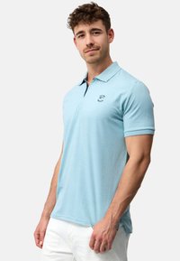 Lys blå polo t-shirt med krave, korte ærmer og et lille logo på brystet. Blødt stof med et simpelt, klassisk design.