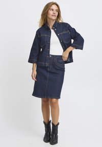 Mörk denimjacka med stora fickor, i kombination med en matchande mörk denimpencilkjol. Vit topp under. Svarta cowboystövlar fulländar looken.