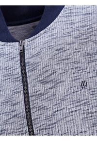 Grå och marinblå zip-up jacka med ett texturerat vävt mönster, ribbad krage och en liten logotypdetalj nära dragkedjan.