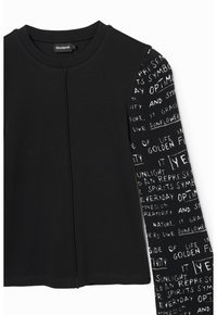 Svart ribbat långärmad topp med mönstrad ärm i kontrasterande färg, prydd med vit text och symboler, som erbjuder en asymmetrisk design.