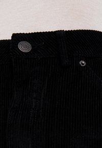 Zwarte corduroy broek met een ribbeltextuur, een metalen knoopsluiting en een klein logo label nabij de tailleband.