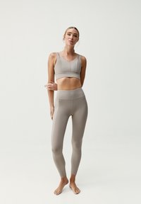 Šviesiai rudos spalvos sportinė liemenėlė ir aukštu juosmeniu kelnaitės, pagamintos iš tamprios, lygaus paviršiaus medžiagos. Liemenėlė turi plačias petnes; be siūlių dizainas komfortui.