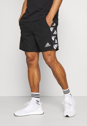 Zwarte sportieve korte broek met wit Adidas-logo en patroonaccenten aan de zijkanten, gecombineerd met witte schoenen en gestreepte zwart-witte sokken.