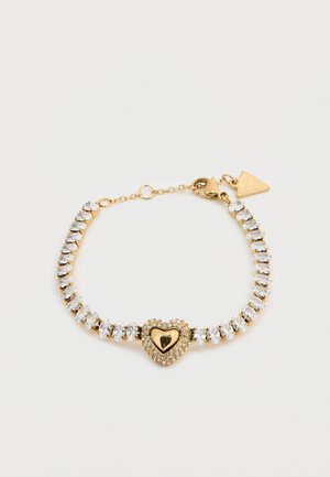 Arany tónusú karkötő, középpontjában szív alakú, fényes felületű dísz, melyet tiszta strasszkövek vesznek körül, finom láncra kapcsolva.