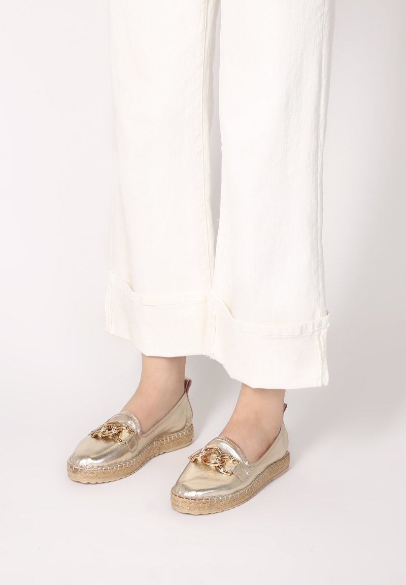Goldene Espadrilles mit Lederoberteil und gewobener Jutesohle; verfügen über ein goldenes Kettenakzent an der Vorderseite und ein rundes Design der Zehenpartie.