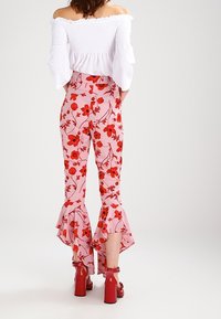 Witte off-shoulder top met gerimpelde bustier, gecombineerd met roze floral-print broek met ruches aan de onderkant en rode chunky hakken.