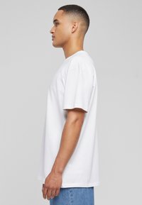 Hvid bomulds T-shirt med korte ærmer, afslappet pasform og rund halsudskæring, vist fra siden mod en neutral baggrund.