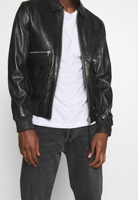 Svart läder bomberjacka med dragkedjestängning, två framsydda fickor med dragkedja, ribbade ärmslut och rundad krage.