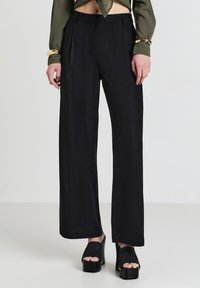 Pantaloni neri a gamba larga realizzati in un tessuto morbido e fluido. Presentano pince sul davanti e sono abbinati a sandali con piattaforma.