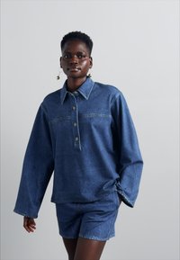 Denim shirt with a buttoned placket, long sleeves, and a casual fit, paired with matching denim shorts. Both in a medium blue wash.