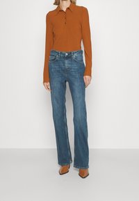 Ribbed, long-sleeve, collar top in burnt orange; paired with straight-leg, dark blue jeans; brown pointed-toe heels.