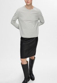 Lichtgrijze lange mouwen shirt gecombineerd met een zwarte leren kokerrok en kniehoog zwart leren laarzen met gouden accenten. Gladde texturen overal.