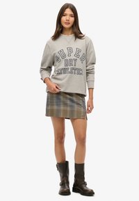 Sweat-shirt gris avec l'inscription "SUPER DRY ATHLETICS", associé à une mini-jupe à carreaux. Bottines en cuir noir avec des boucles décoratives.