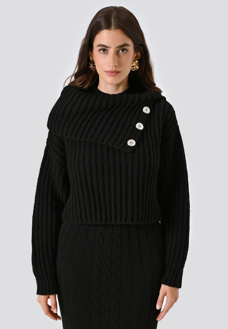 Maglione a costine nero con colletto ampio e ripiegato, caratterizzato da quattro bottoni decorativi sulla spalla, abbinato a una gonna in tessuto coordinato.