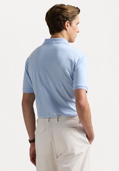 Tricou polo cu mânecă scurtă, de culoare bleu deschis, cu guler clasic, textură netedă și un croi ușor ajustat, asortat cu pantaloni de culoare crem.