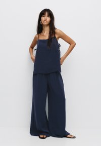 Completo in misto lino di colore blu navy, leggero, composto da un top corto senza maniche con dettagli a laccio e pantaloni larghi e morbidi.