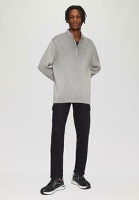 Grijze geribbelde pullover met een kwart-rits kraag, gecombineerd met zwarte cargobroek en zwarte sportschoenen. Casual, relaxte pasvorm en textuur.