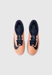 Nike Vapor Pro sportbačiai su oranžine tinklelio viršūne, tamsiai mėlynomis detalėmis, briaunota tekstūra ir išlenktu šviesiai mėlynu padu. Kraujo užsegimas.