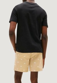Czarna bawełniana koszulka z okrągłym dekoltem, zestawiona z beżowymi szortami z jasnym geometrycznym wzorem. Materiał wydaje się gładki i lekki.
