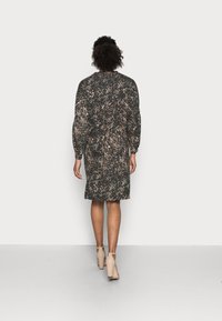 Robe avec un motif abstrait noir et beige, à manches longues, longueur genou, coupe décontractée, taille élastique, associée à des sandales à talons beiges.