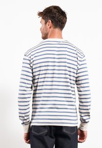 Langermet stripet skjorte i hvit og blå, laget av mykt stoff, med mansjetter og rund hals. Synlige sømmer og avslappet passform.