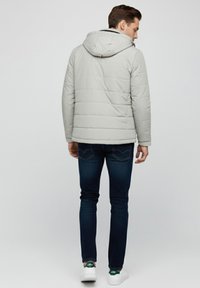 Chaqueta acolchada gris claro con capucha, con costuras diagonales. Combinada con vaqueros azul oscuro y zapatillas blancas con detalles verdes.