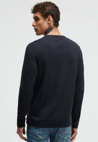 Langärmliges, nachtblaues Hemd aus einem weichen, strukturierten Stoff. Rundhalsausschnitt und anliegende Ärmel, mit einer dezenten Naht an der Schulter.