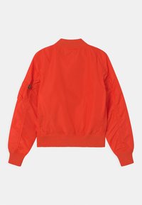 Red nylon bomber jacket with a ribbed collar and cuffs, features gathered detailing on the sleeves, and a zippered pocket on the arm.