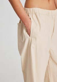 Pantaloni bej, ușori, cu croi lejer, cu talie elastică și buzunar lateral, având o textură netedă și un design cu picior drept.