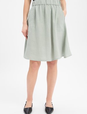 Femme portant une jupe gris clair mi-longue avec une taille élastique et des poches latérales, associée à des chaussures slingback noires à bout pointu.