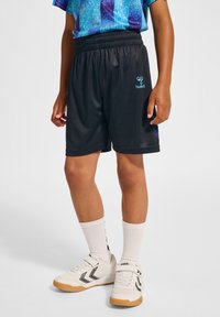 Svarta sportshorts gjorda av slät tyg, med elastisk midjeband och blå logodetalj. Bärs med vita skor och strumpor.