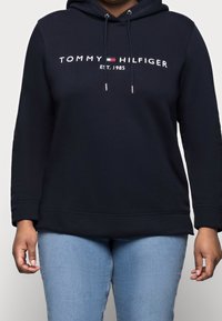 Tmavě modrá mikina s kapucí z bavlněné směsi, na přední straně s bílým logem „TOMMY HILFIGER EST. 1985“ a nastavitelné šňůrce na kapuci.