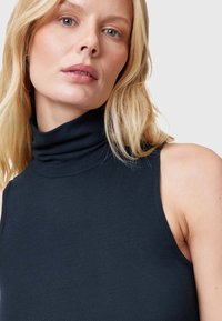 Top negro de cuello alto con textura acanalada y diseño sin mangas. Primer plano que muestra el detalle del cuello y la exposición de los hombros.