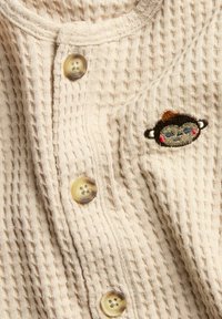 Beige katoenen cardigan met ribbelstructuur, voorzien van vier ronde knopen en een klein geborduurd aapje ontwerp op de linkerborst.