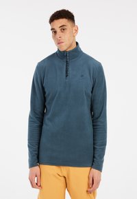 Pullover in pile blu scuro con colletto a mezza zip, caratterizzato da una texture a coste e una stampa del logo lungo la zip. Maniche lunghe.
