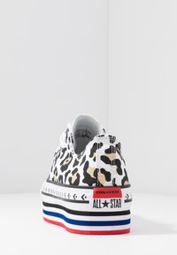 Sneaker low-top Converse All Star con stampa leopardata nera, beige e bianca e suola spessa con strisce rosse, blu e nere, vista da dietro.