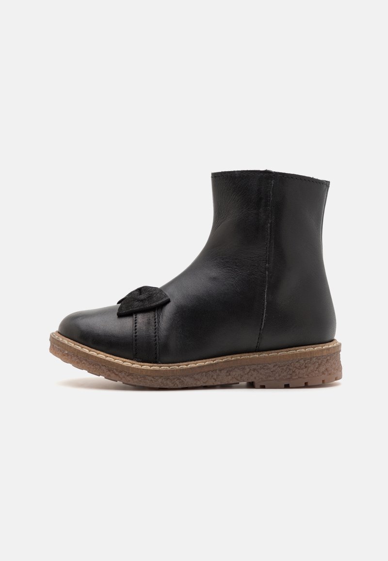 Bottine en cuir noir à bout rond, avec un nœud décoratif à l'avant et une semelle en caoutchouc marron texturée avec une couture beige.
