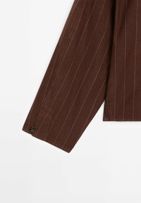 Chemise marron à manches longues avec de fines rayures blanches verticales et un seul bouton foncé au niveau du poignet sur fond blanc.