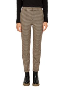 Vrouw in slanke beige en zwarte houndstooth broek, gecombineerd met een zwart langemouwen top en zwarte enkellaarzen met beige zolen.
