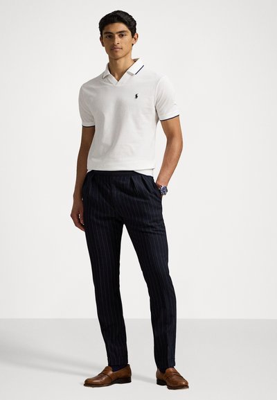 T-shirt polo blanc avec des accents marine, associé à un pantalon rayé foncé et des chaussures en cuir marron. La chemise comporte un col et un logo.