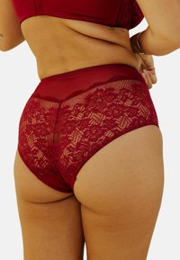 Slip taille haute en dentelle bordeaux avec des détails floraux et en tissu en maille lisse, présentant un bord festonné sur le dessus.