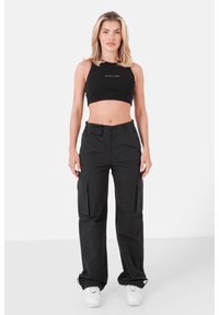 Top corto nero con logo, abbinato a pantaloni cargo neri con ampie tasche laterali e una vestibilità comoda, completato da sneakers bianche.