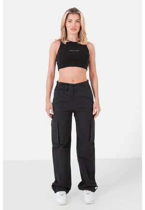 Schwarzes, kurzes Tanktop mit Logo, kombiniert mit schwarzen Cargo-Hosen mit großen Seitentaschen und einer lässigen Passform, ergänzt durch weiße Sneakers.