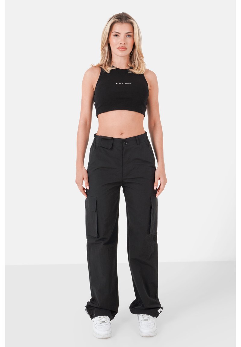 Top corto nero con logo, abbinato a pantaloni cargo neri con ampie tasche laterali e una vestibilità comoda, completato da sneakers bianche.