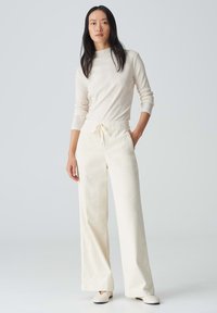 Lichtbeige langemouwtop met een subtiele textuur en een opstaande kraag. Gecombineerd met crème wijde broek met een elastieken tailleband en een trekkoord.